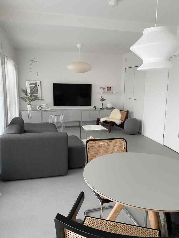 モノトーンのリビング、グレーのソファとテレビ台、ラウンドテーブルと木製のアームチェアが配置されたシンプルな空間