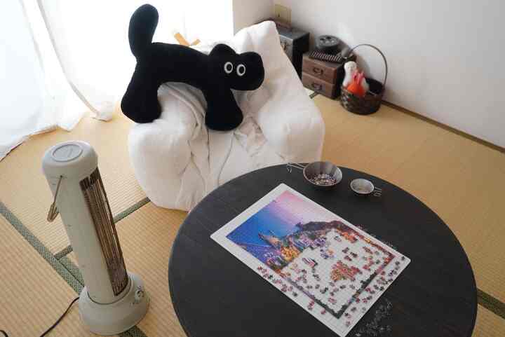 Bright white and brown tatami room featuring a plush white armchair with a black cat cushion, a round black table with puzzle pieces creating a cozy atmosphere