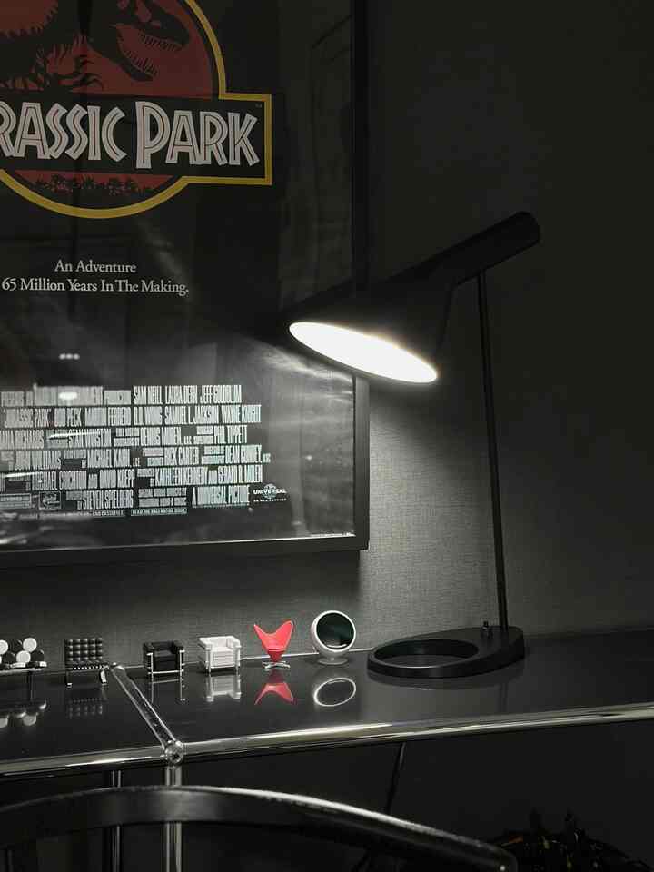 Modern black-toned home office featuring a black table lamp and Jurassic Park poster with sleek atmosphere