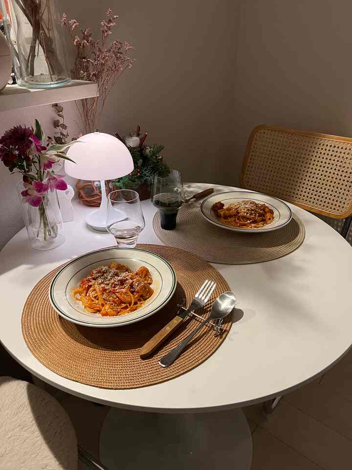 白と木目調が調和する二人用ダイニング、ラタンチェアとテーブルランプが配置されたシンプルで自然な雰囲気の空間