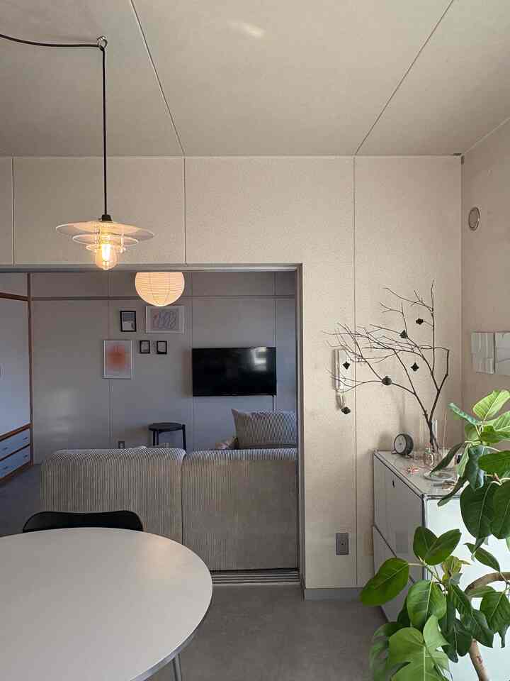 ベージュとグレーの色調の3DKリビングとダイニングスペース、ソファ、丸テーブル、ペンダントライト、植物が配置された印象的でナチュラルなインテリア