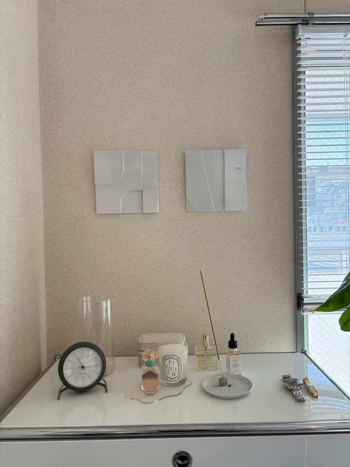 A minimal and natural space with beige walls and white cabinet topped with clock, candle, diffuser, and decor items