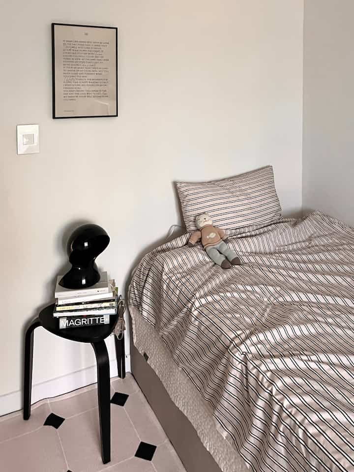 Simple bedroom with white walls and black side table, featuring striped bedding and pillow in a cozy setting