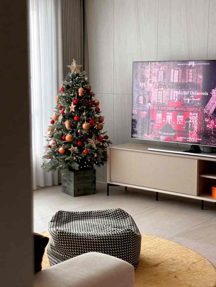 ナチュラルトーンのリビング、クリスマスツリーとラウンドラグ、モノトーンのプーフが配置された雰囲気のあるインテリア