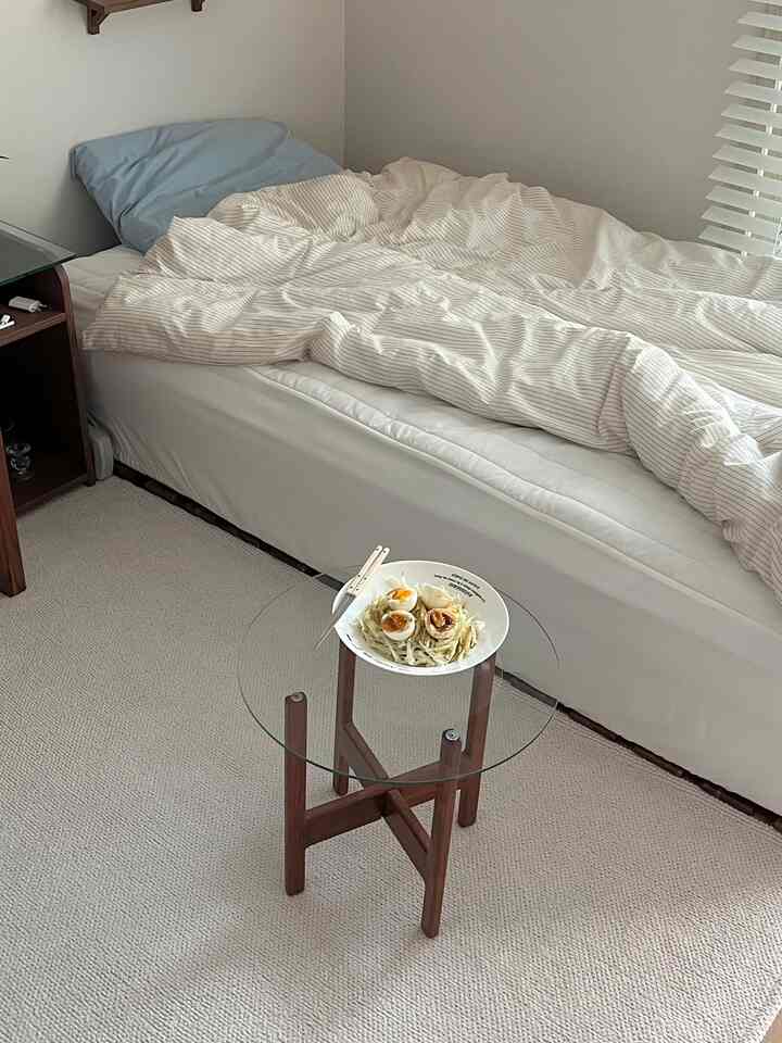 明るい白と木目調が調和したワンルームの寝室、ベッドとガラストップのダイニングテーブルがすっきり配置された印象的な空間