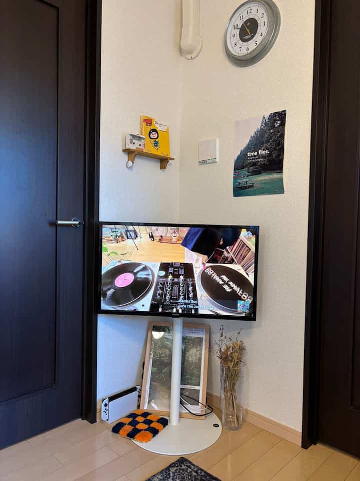 A cozy living room corner with modern white TV stand between black doors, featuring a wall clock and minimalist decor