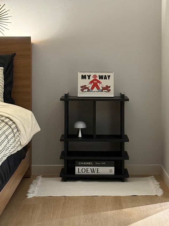 Simple bedroom nightstand area with beige wood tone flooring and black shelving unit