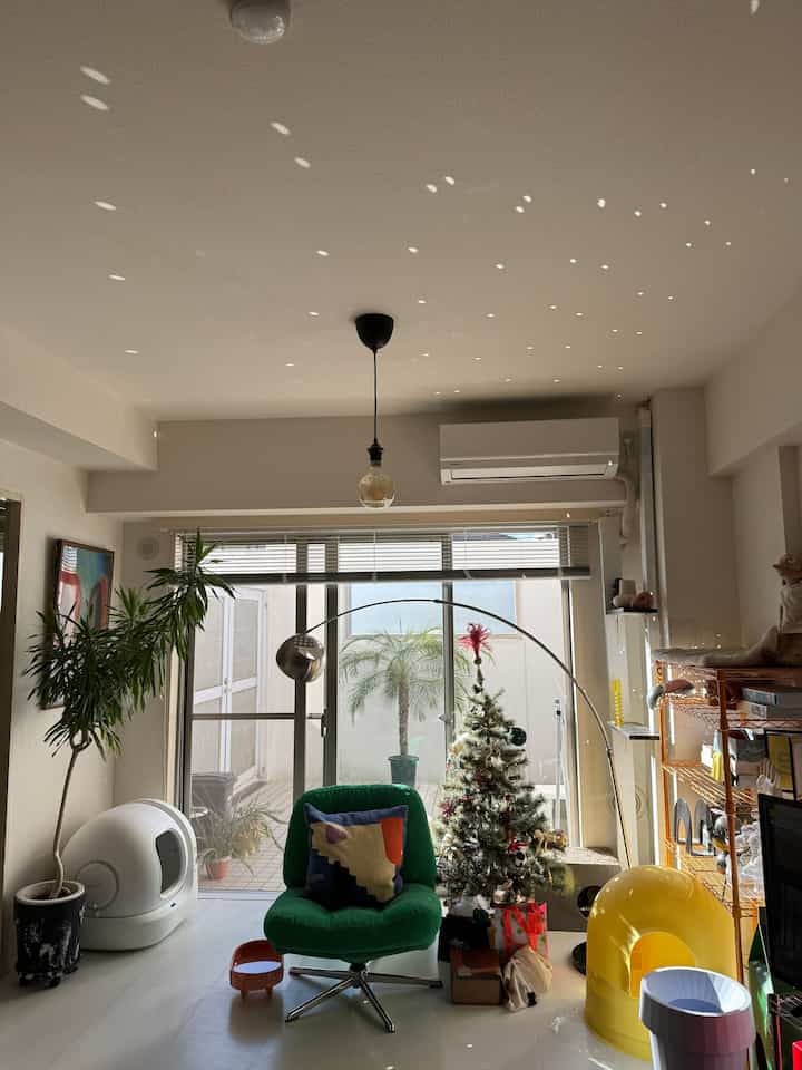 白を基調としたリビング、緑のアームチェアや猫用具、植物が配置されたミッドセンチュリーモダンの雰囲気あるインテリア