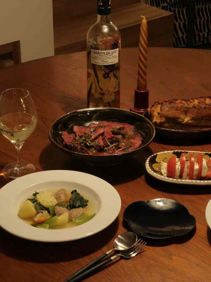 温かみのあるブラウンのダイニングルーム、木製のテーブルに様々な料理とワイングラス、ツイストキャンドルが配置された雰囲気のあるホームパーティー空間