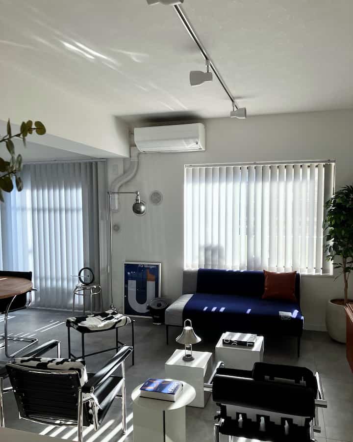 White walls and blinds with Mid-Century Modern sofa and black leather chairs in a stylish living room
