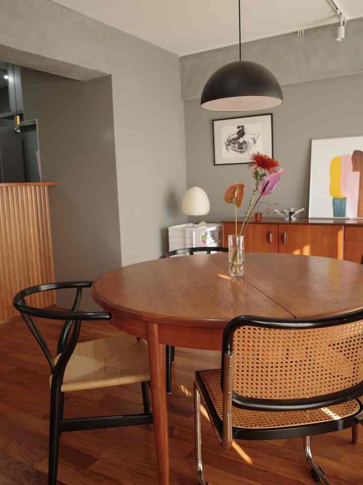 ブラウンとブラックのトーンが調和した4人用ダイニングルーム、木製のラウンドテーブルと椅子、ペンダントライトとアートポスターが配されたモダンな雰囲気のインテリア