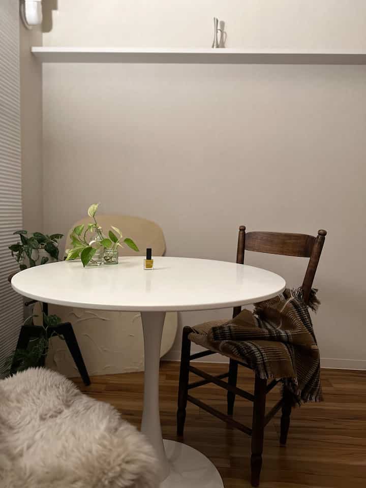 白と茶色の色調のダイニング、丸いダイニングテーブルと木製の椅子、テーブルの植物と温かみのあるブランケットが配置された自然な雰囲気のあるインテリア