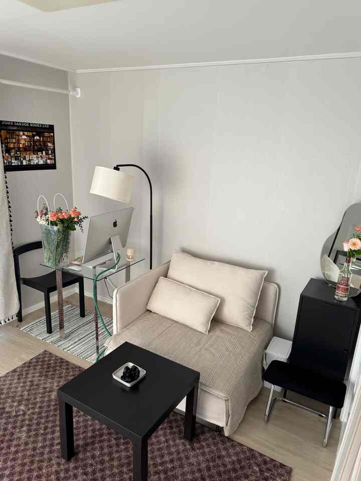 ベージュとブラックの色調のコンパクトなワンルームホームオフィス、クリーム色のソファとガラスのデスクが配置されたシンプルなインテリア