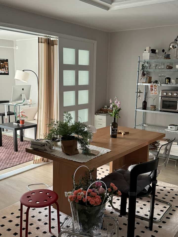 ナチュラルなブラウンとホワイトトーンのワンルームリビング、木製テーブルと植物、金属棚が配置された雰囲気のある空間