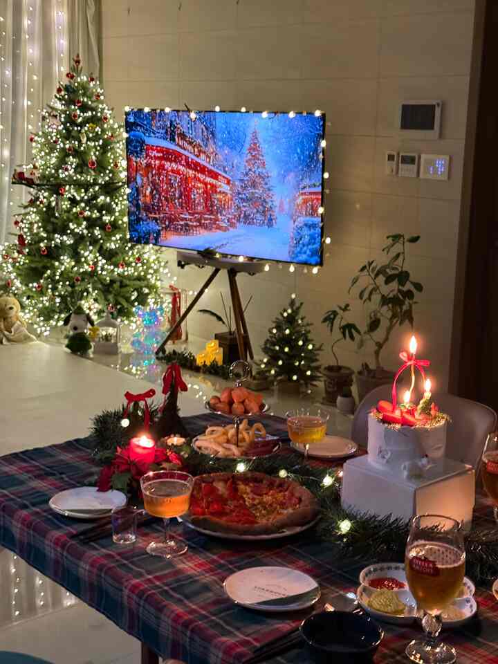 白い壁と床のリビング、クリスマスツリーと照明で飾られたテーブルに料理とケーキが置かれた雰囲気のあるホームパーティースペース