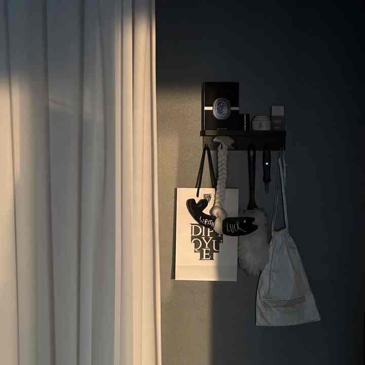 白いカーテンと黒い壁の対比が美しい、ミニマルな壁掛け棚に雑貨が置かれた自然光のある落ち着いた空間
