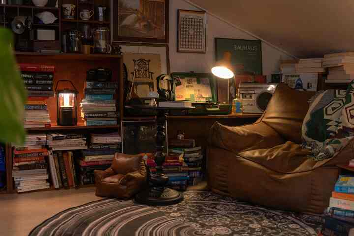 暖かみのあるブラウンのトーンのリビングルーム、ビーンバッグソファと多数の本棚、テーブルランプが配置されたヴィンテージ風インテリア