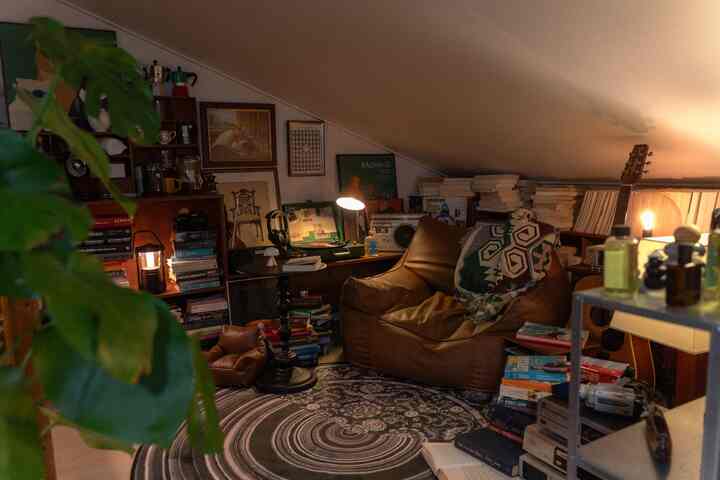 暖かいブラウン調のロフトワンルームの音楽ゾーン、レザーのビーンバッグソファと丸いラグ、ヴィンテージ照明と本棚が雰囲気あるインテリア