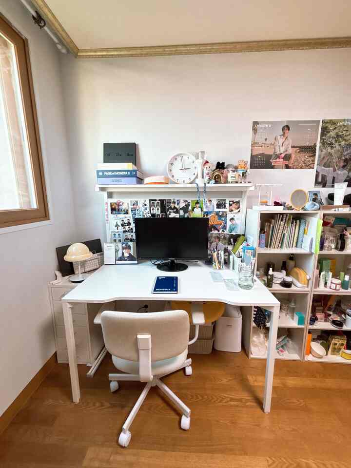 白を基調としたホームオフィス空間。広いデスクとオフィスチェア、棚の上の時計や多くの写真立てと小物が配置された整頓された作業環境