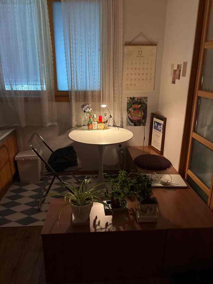 白と木目調が調和するワンルームのホームカフェ、透明な折りたたみ椅子と植物が配された落ち着いた雰囲気のインテリア