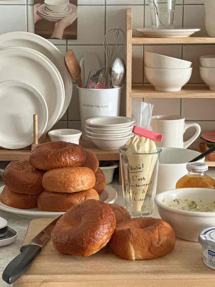 ナチュラルなベージュとホワイトウッドのキッチン、ベーグルとベーキング道具が配置された落ち着いたホームカフェの雰囲気のあるインテリア