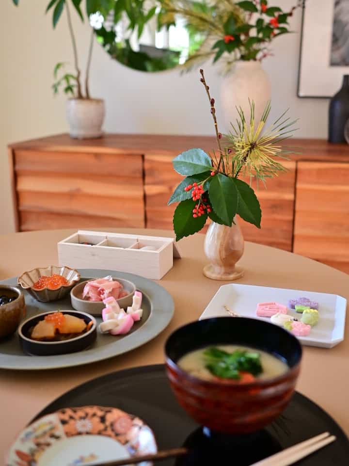 ベージュ色調のダイニング、木製サイドボードと和食器、季節の花飾りが配置された落ち着いた雰囲気のインテリア