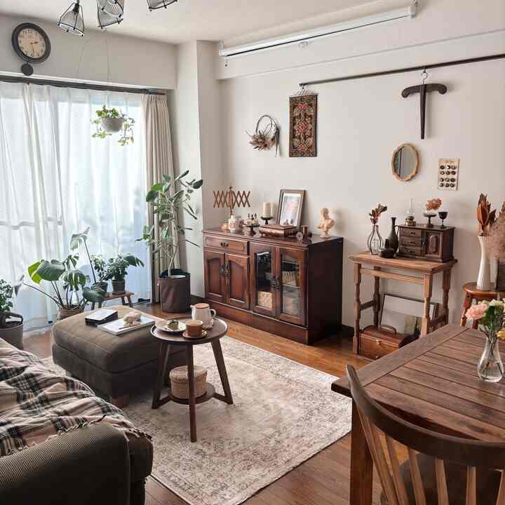 ブラウンの木目調リビング、ヴィンテージ家具とダイニングテーブル、植物と陽光が調和した雰囲気のあるインテリア