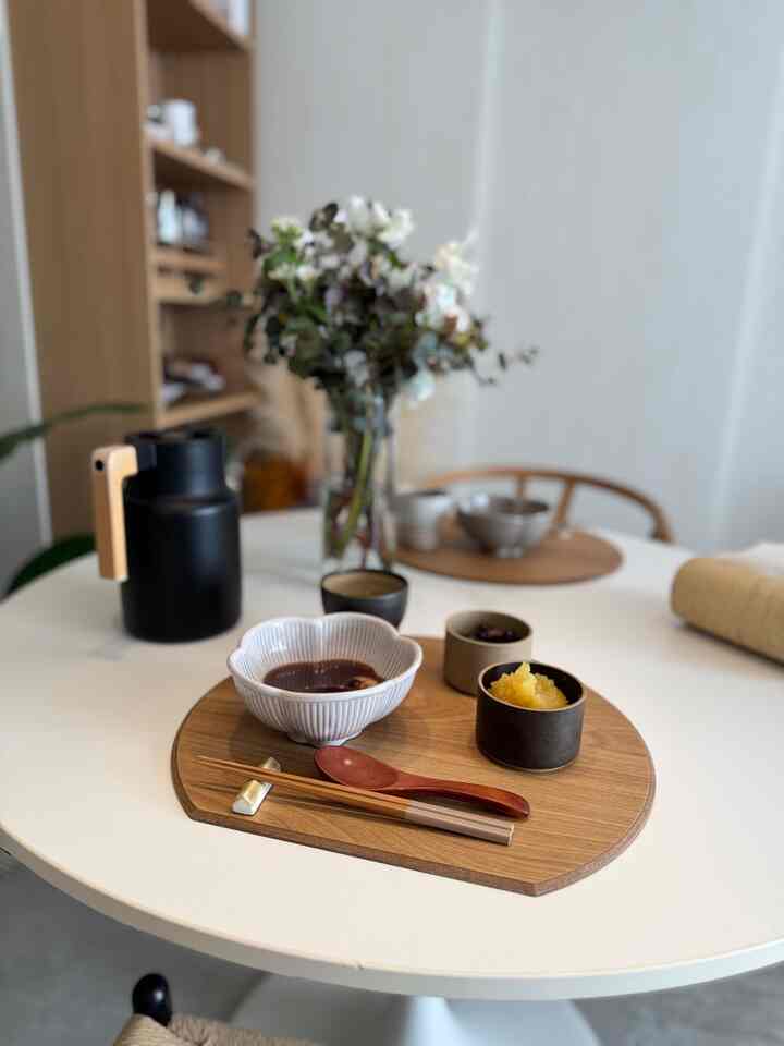 ナチュラルカラーの円形ダイニングテーブル、木製ランチョンマットと和食器、花瓶が配置された印象的なダイニングインテリア