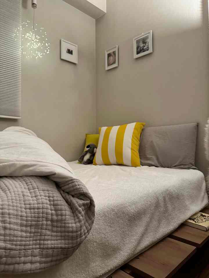 A small bedroom with beige and natural tones featuring a wood-tone bed frame and yellow cushions creating a cozy atmosphere