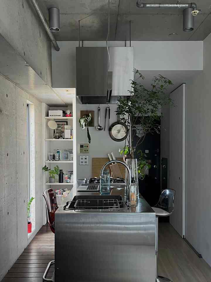 ナチュラルカラーのワンルームキッチン、ステンレス製アイランドと透明な椅子が配置された自然感じのある空間