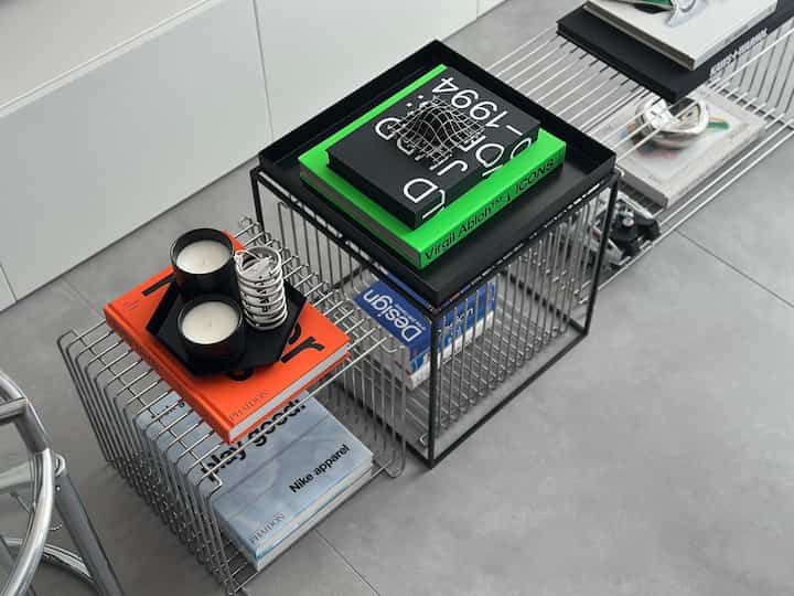 Modern space with black wire side tables and gray floor, featuring trays, books, and candles neatly arranged