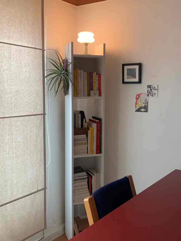 白と赤の色調のリビング、隙間収納の本棚とネイビーのアームチェアが配置された雰囲気のある空間