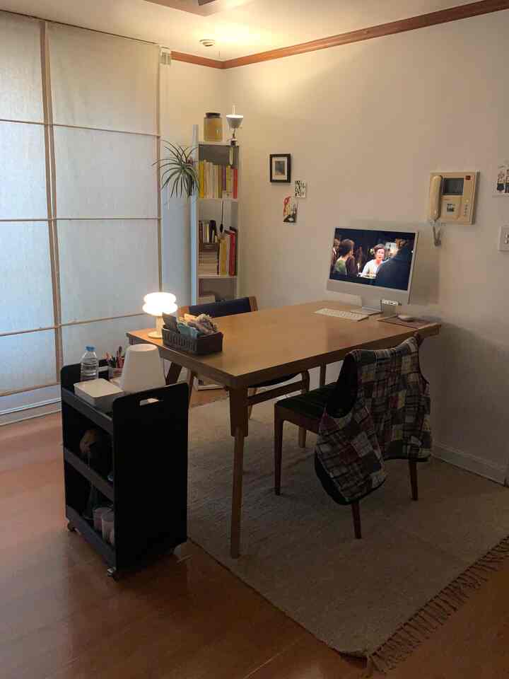 木目調とベージュの調和が取れたリビングダイニング、狭い白い本棚と木製テーブルが配置された雰囲気のある空間