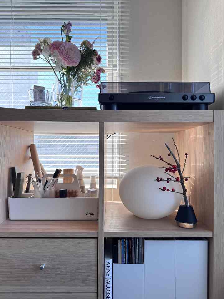 ナチュラルな木目調とホワイトが調和したリビングの本棚に、レコードプレーヤーと花瓶が配置された印象的なミッドセンチュリーモダンなインテリア