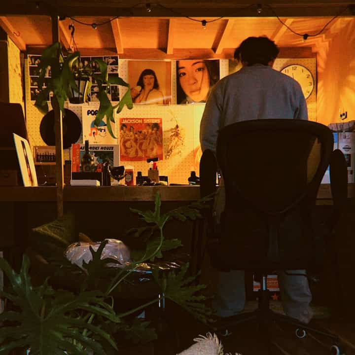 暖かいオレンジ色調のホームオフィス、壁にポスターと時計、机の上にDJ機材と植物が配置された雰囲気のある空間