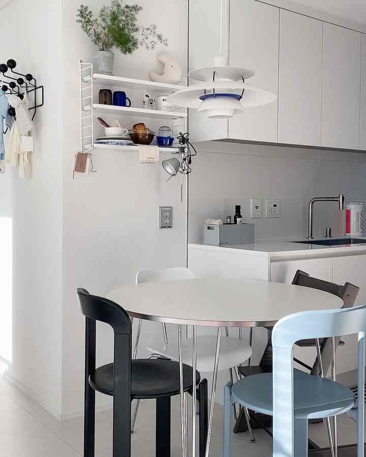 White-toned small kitchen featuring a round dining table, wall shelves, and pendant lighting in a clean modern space