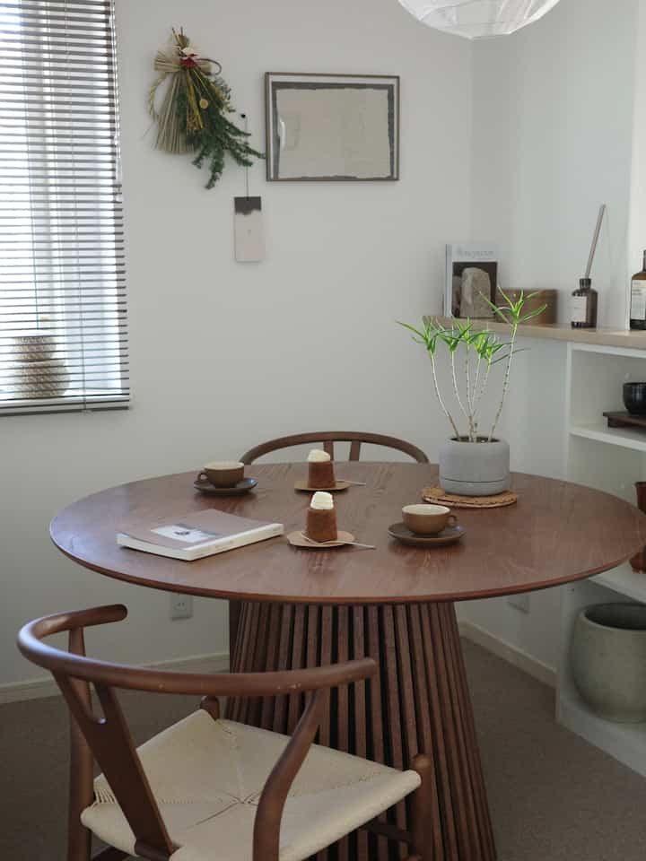 落ち着いたナチュラルな木目調と白い壁のダイニング、丸いテーブルと椅子に植物やディフューザーが配置された雰囲気のある空間