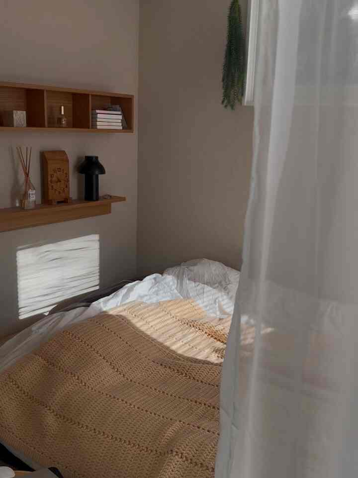 Natural beige and wood tone bedroom featuring white sheer curtain and knitted blanket creating a cozy atmosphere