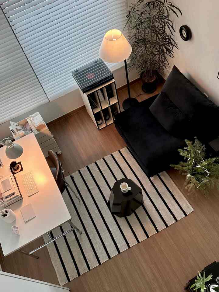 Wood tone flooring with white blinds complements a minimal home office and living room for a single occupant