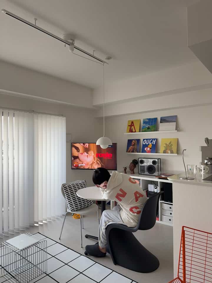 白とモダンな色調のリビング、丸いテーブルと黒のアームチェア、縦型カーテンが配置された雰囲気のあるインテリア