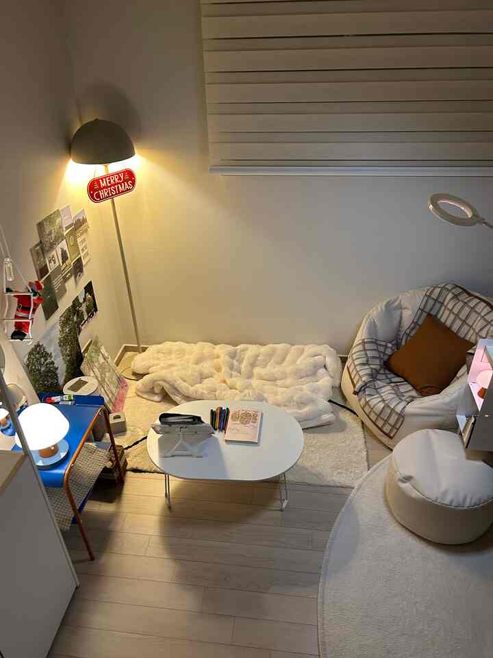 White-toned small living room with warm lighting, featuring a blanket, bean bag chair, and compact table creating a cozy setting
