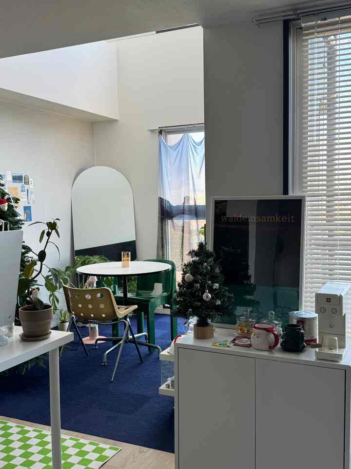 White and navy toned studio apartment dining space featuring a round dining table, chairs, arched mirror, plants, and coffee machine with a neat atmosphere