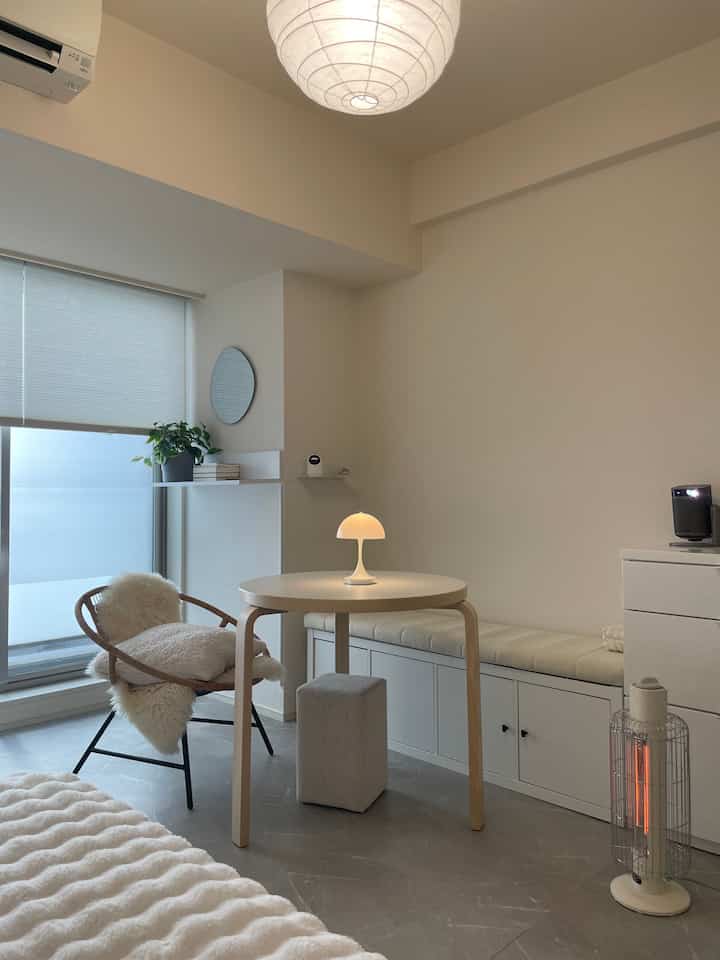 Bright white and natural toned studio living room featuring a round table, chair, and bench in a simple setting