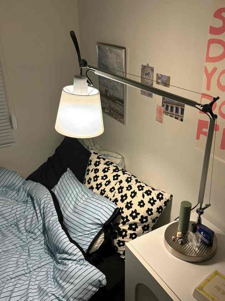 ホワイトとブルーのトーンの寝室、ストライプの寝具と花柄の枕が配置されたベッドとナイトテーブルの上の照明がある雰囲気のある空間