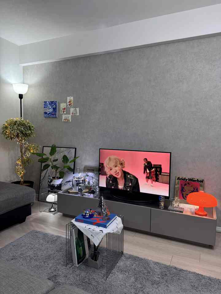 グレーの壁と木目調の床が特徴のミッドセンチュリーモダンなリビング、グレーのソファとワイヤーフレームのコーヒーテーブルが配置された落ち着いた雰囲気のインテリア