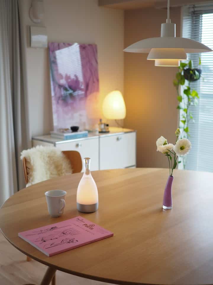 White and wood tone natural modern dining room featuring a large round dining table, pendant light, and vase with flowers creating a cozy atmosphere