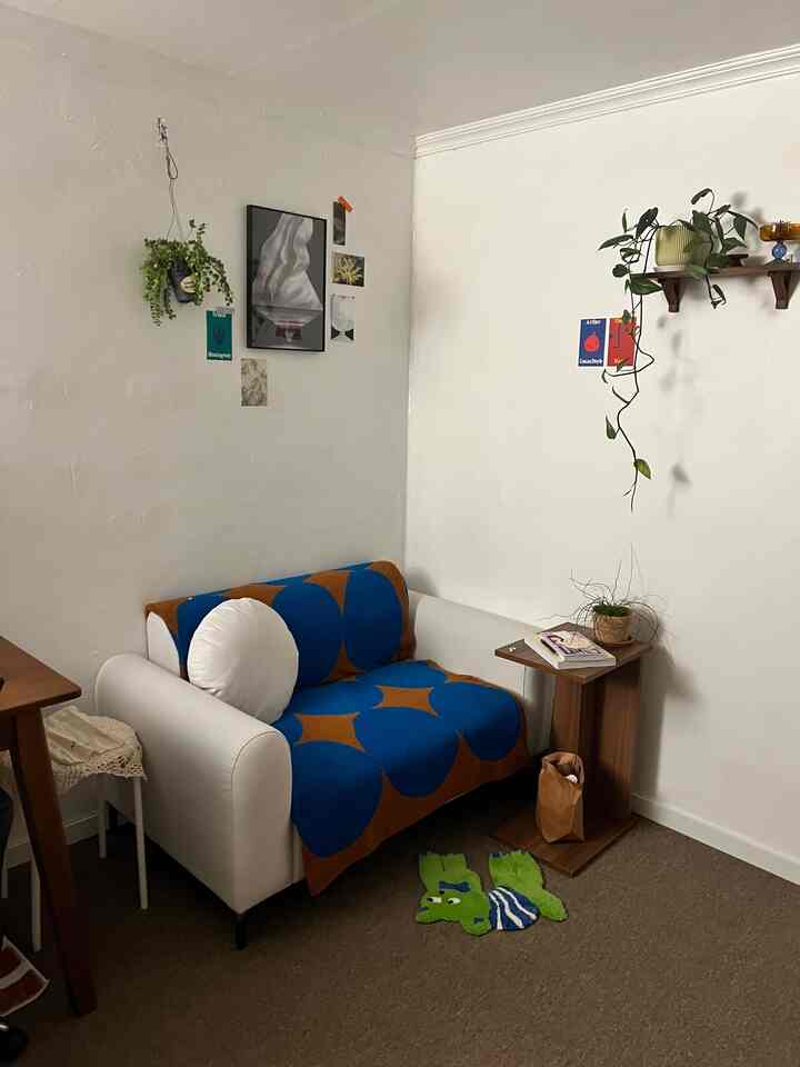 白い壁とベージュのカーペットがある、ソファとサイドテーブルを備えた落ち着いた二人用読書スペース