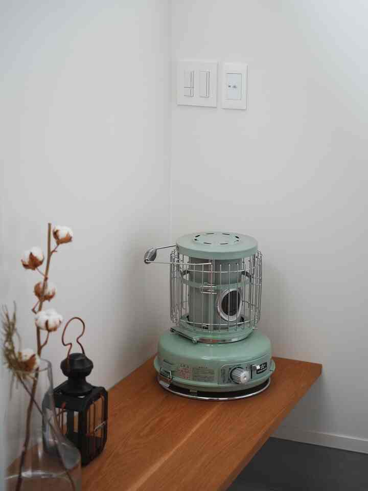 Minimal corner space with white walls and natural wood-tone table, featuring a small green heater and decorative lantern