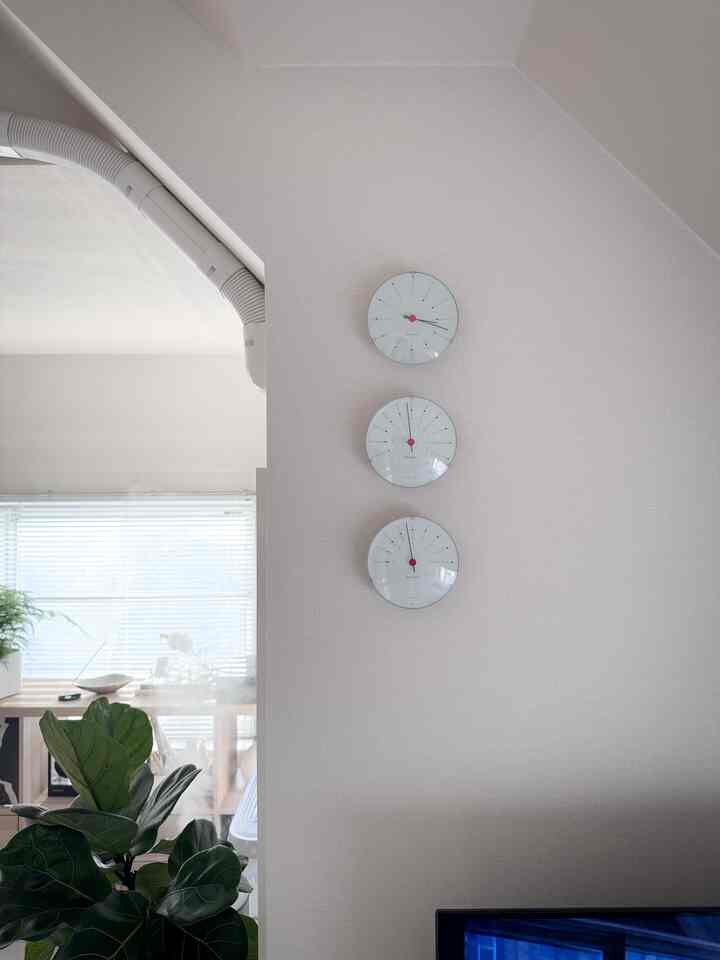 明るく自然な色調の空間に、壁に配置されたアルネヤコブセンの時計と緑の植物が調和したミッドセンチュリーモダンスタイルのインテリア