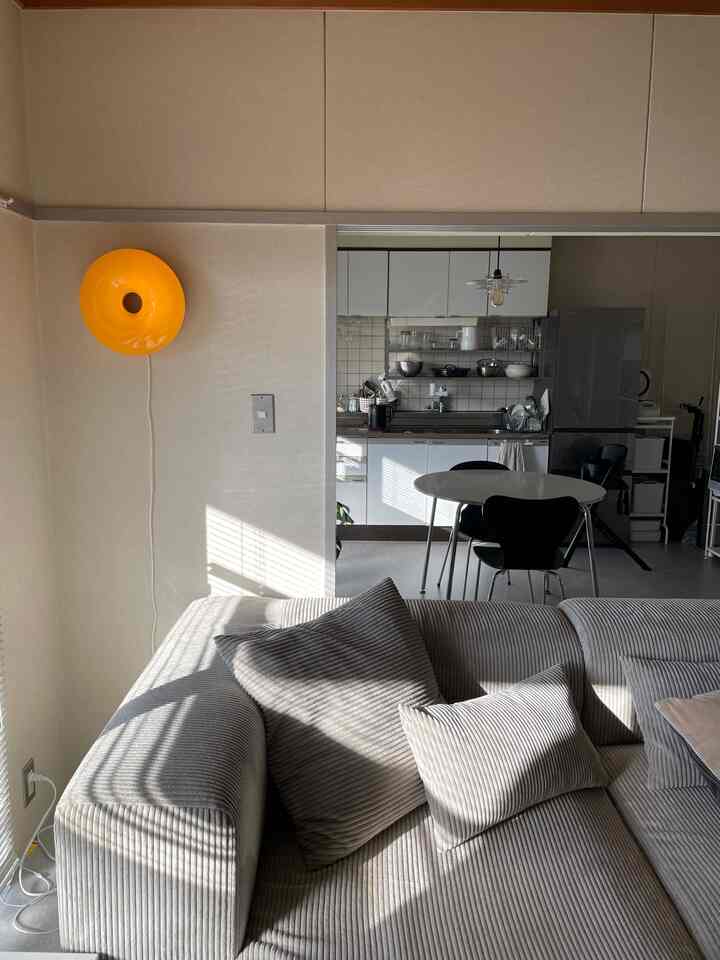 A 3DK apartment living and kitchen space featuring light beige walls and gray corduroy fabric sofa with minimalist dining table